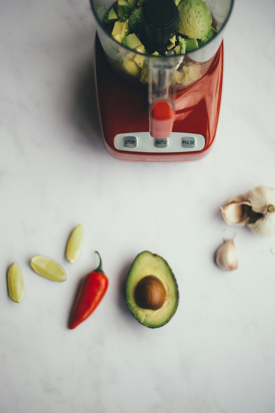 Rote Küchenmaschine mit Avocado, Limette und Chili daneben.